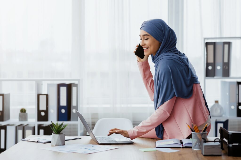 Muslim Business Lady Talking On Cellhone And Using Laptop In Office
